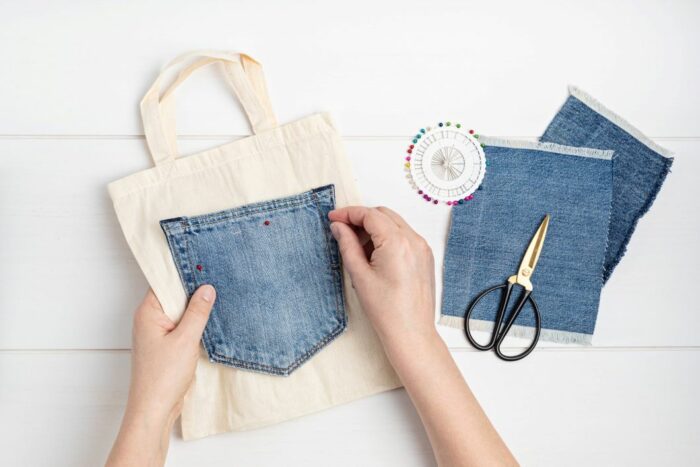 person sewing denim pocket onto a bag